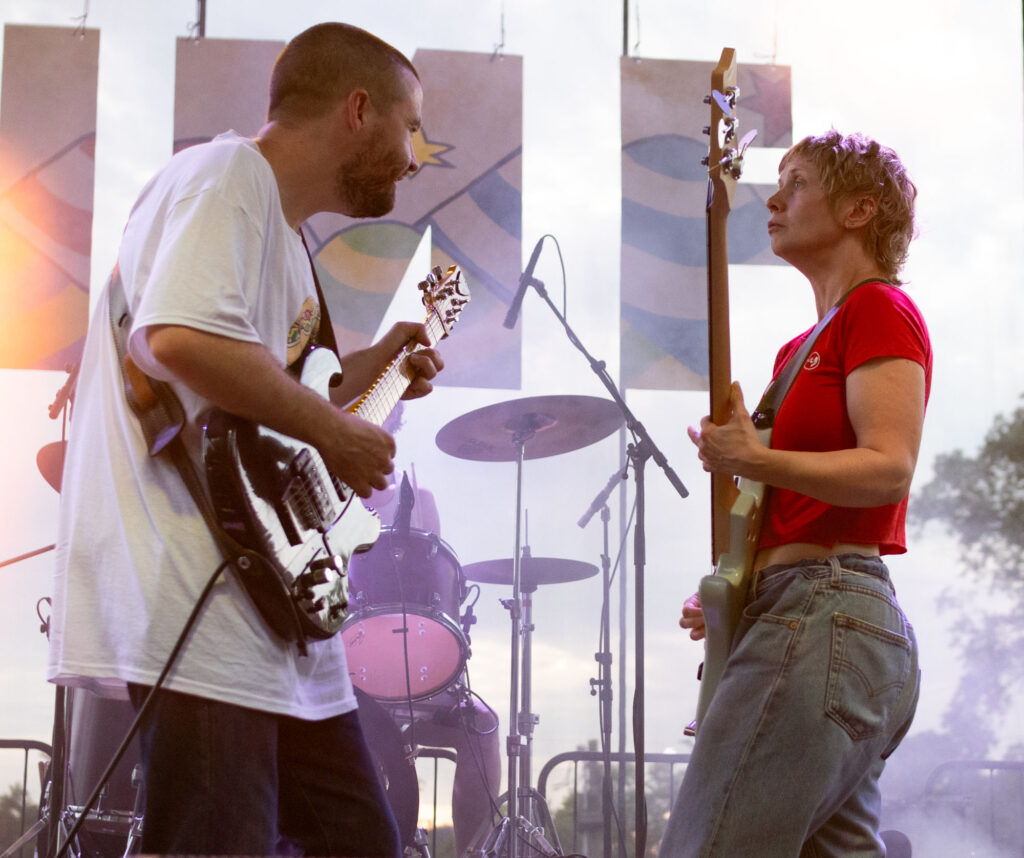Guitarist and bassist playing on stage standing in front of each other.