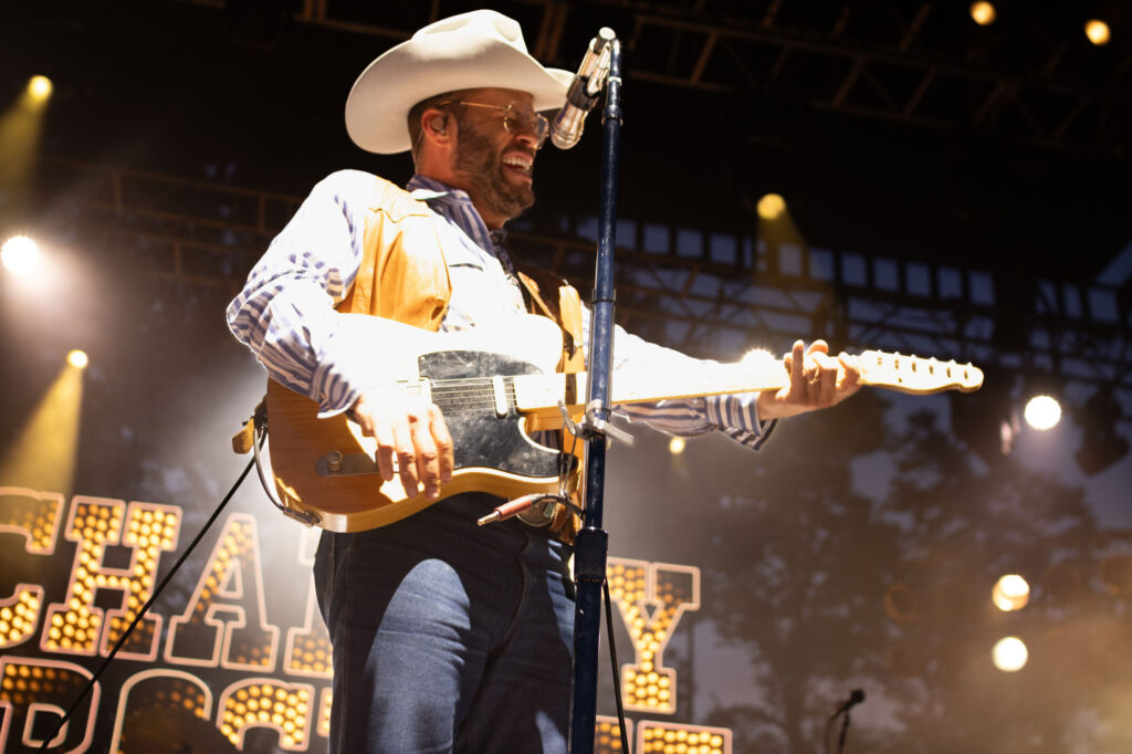 Man playing a guitar, wearing a cowboy hat, singing on stage