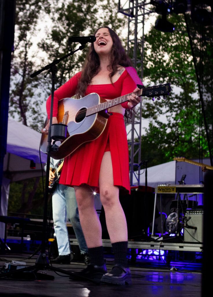 Woman playing acoustic guitar and singing on stage. 
