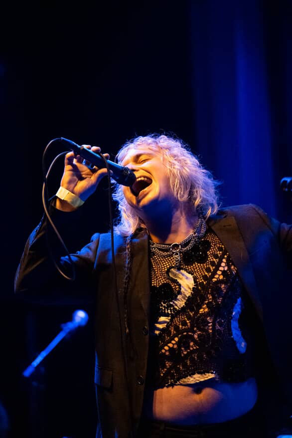 Mothe singing into a microphone, with eyes closed and light shining on their face. 