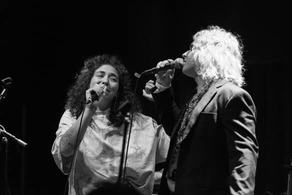 Indigo De Souza and Mothe singing on stage. Both holding microphones and looking at each other.