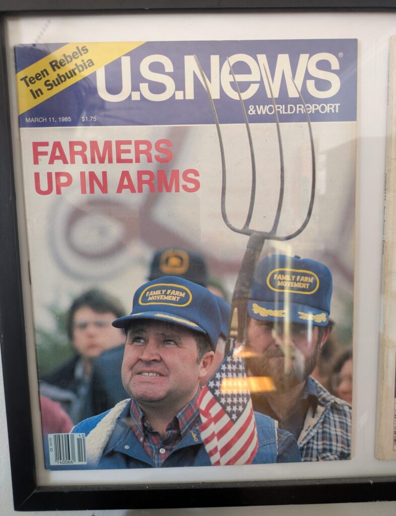 U.S. News magazine framed with headline "FARMERS UP IN ARMS" showing a man with a blue hat with yellow words that read "Family Farm Movement," holding a small American flag. A man behind him has the same hat and is holding a pitchfork.